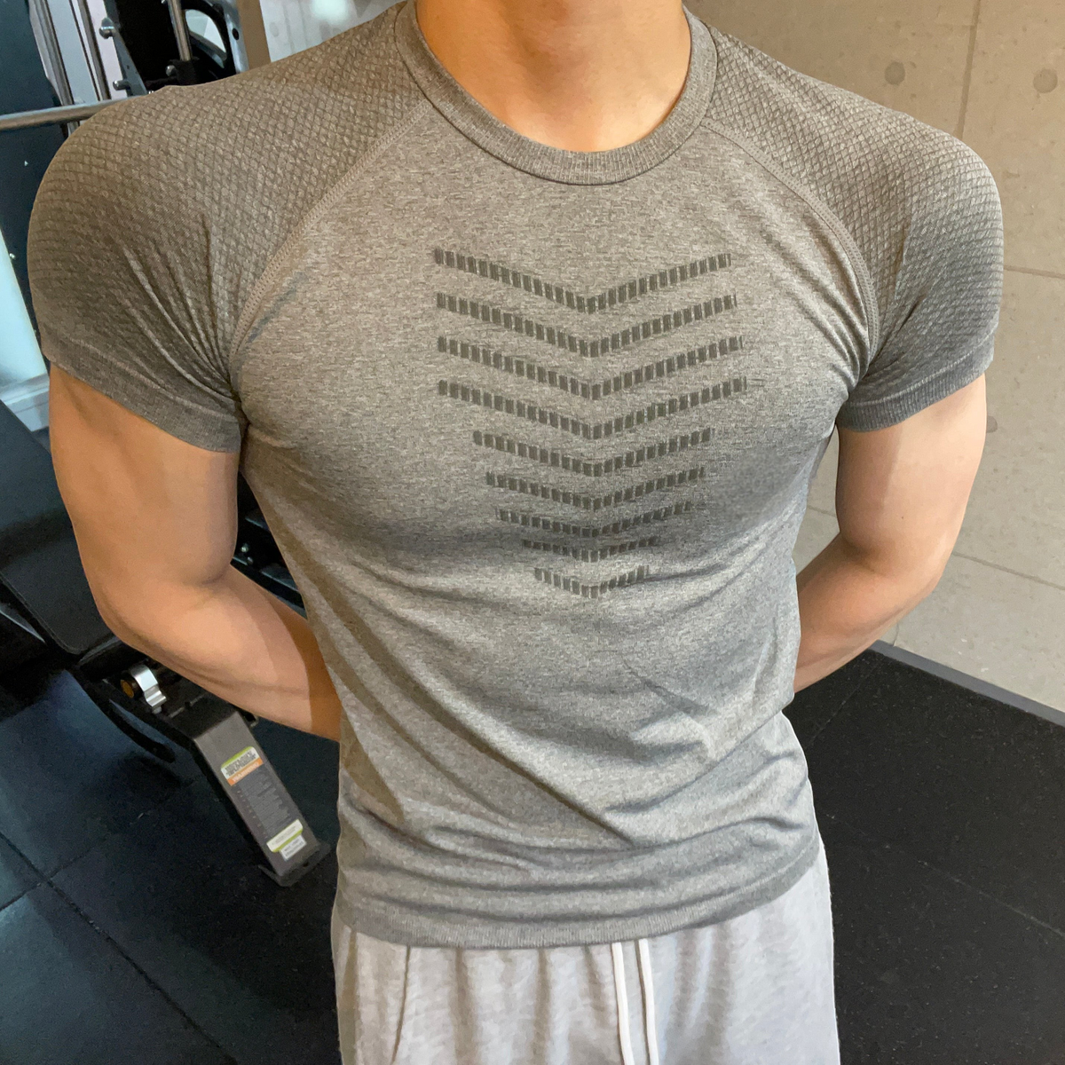 ASCEND gray seamless compression t-shirt with scale pattern detail worn by a muscular man in a gym setting