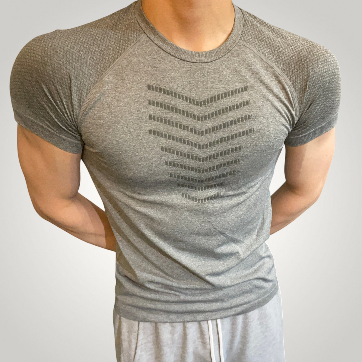 ASCEND gray seamless compression t-shirt with scale pattern detail worn by a muscular man in a gym setting